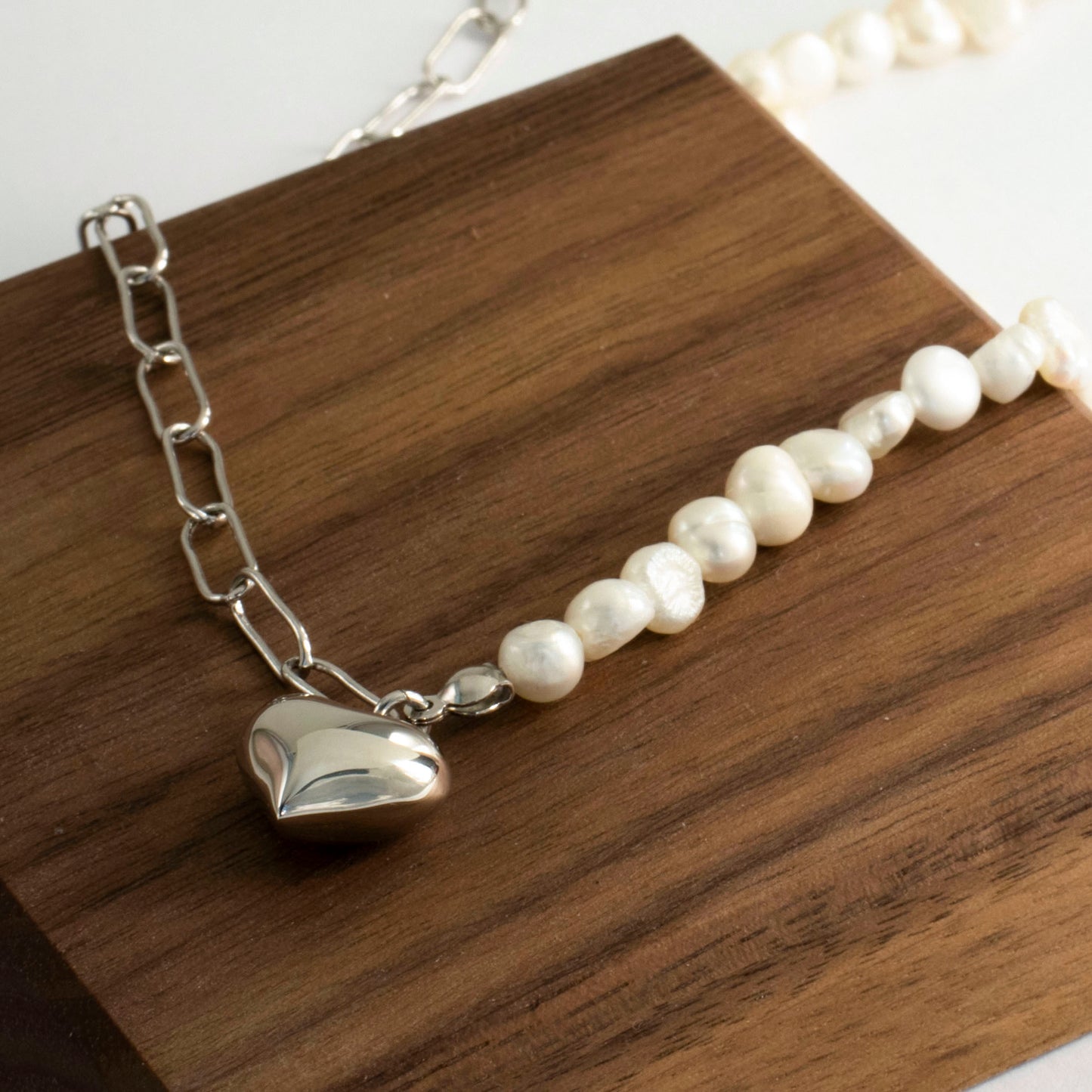 This stylish piece features a half chain with baroque pearls and other half an alta chain with a heart pendant.