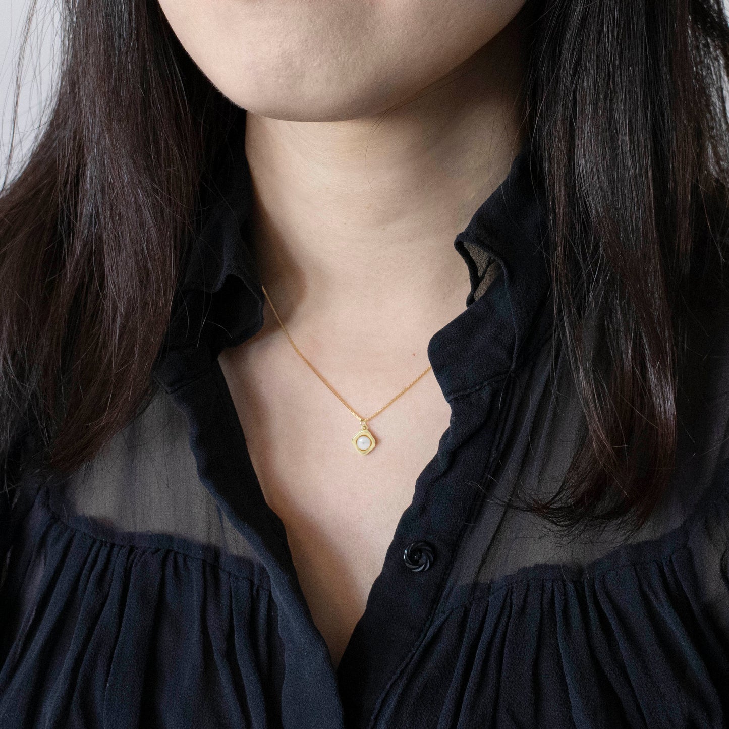 A rhombus pendant embracesa button pearl, featuring an engraved reverse side with the inspiring mantra 'Never give up.'
