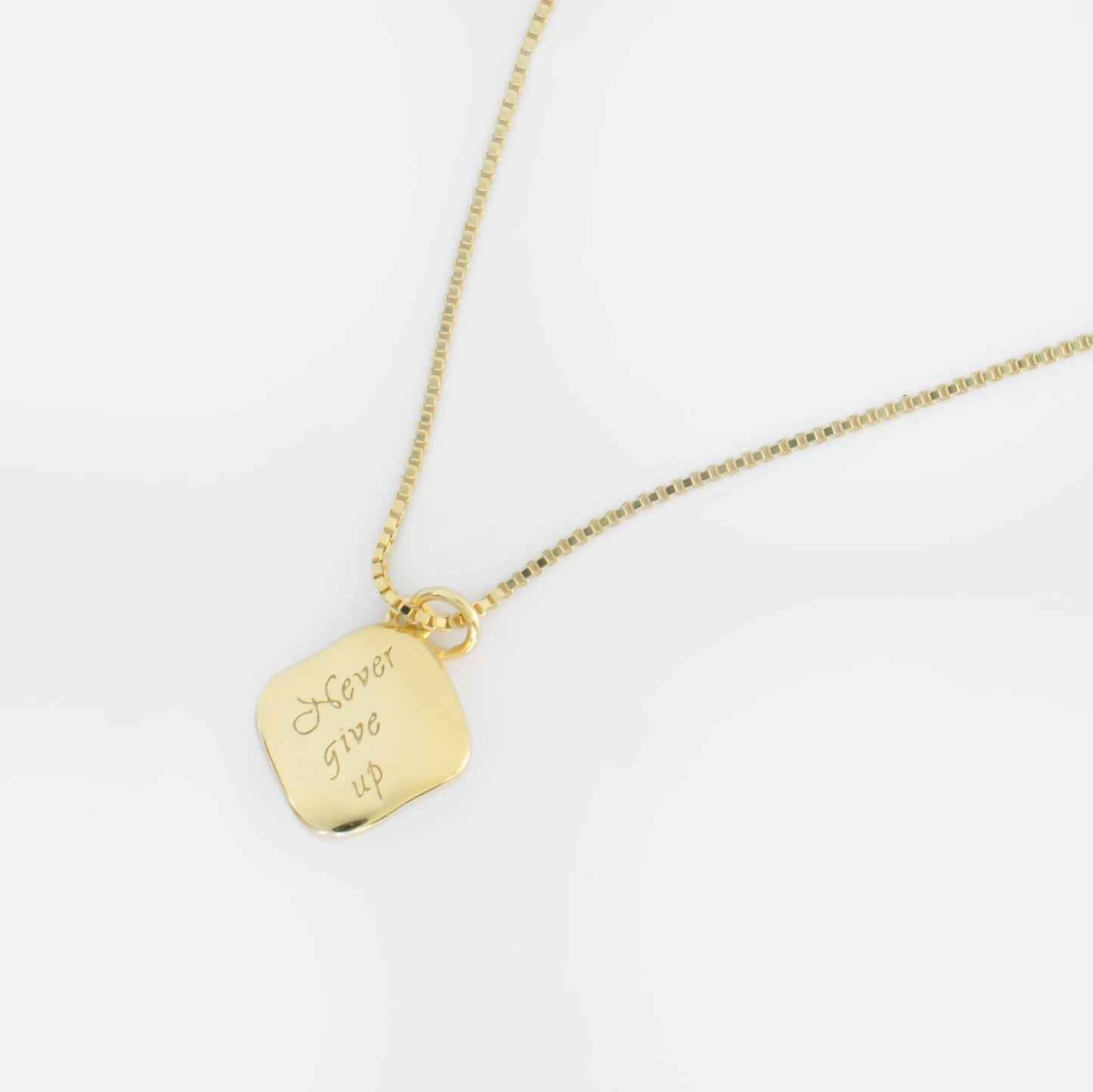 A rhombus pendant embracesa button pearl, featuring an engraved reverse side with the inspiring mantra 'Never give up.'