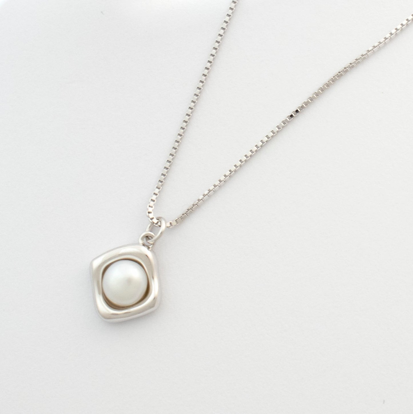 A rhombus pendant embraces a button pearl