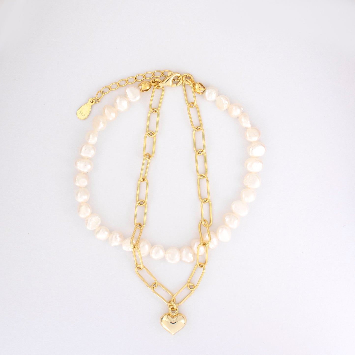 This stylish piece features a dual chain with baroque pearls and an alta chain with a heart pendant.