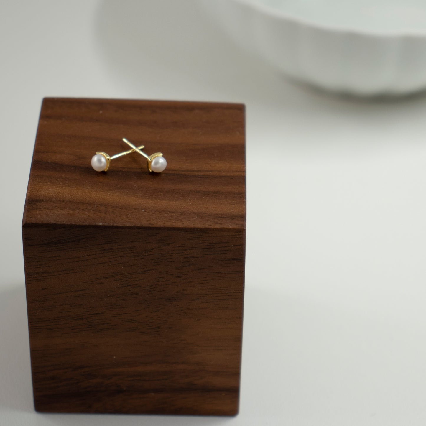 A rhombus stud earring embraces a button pearl.
