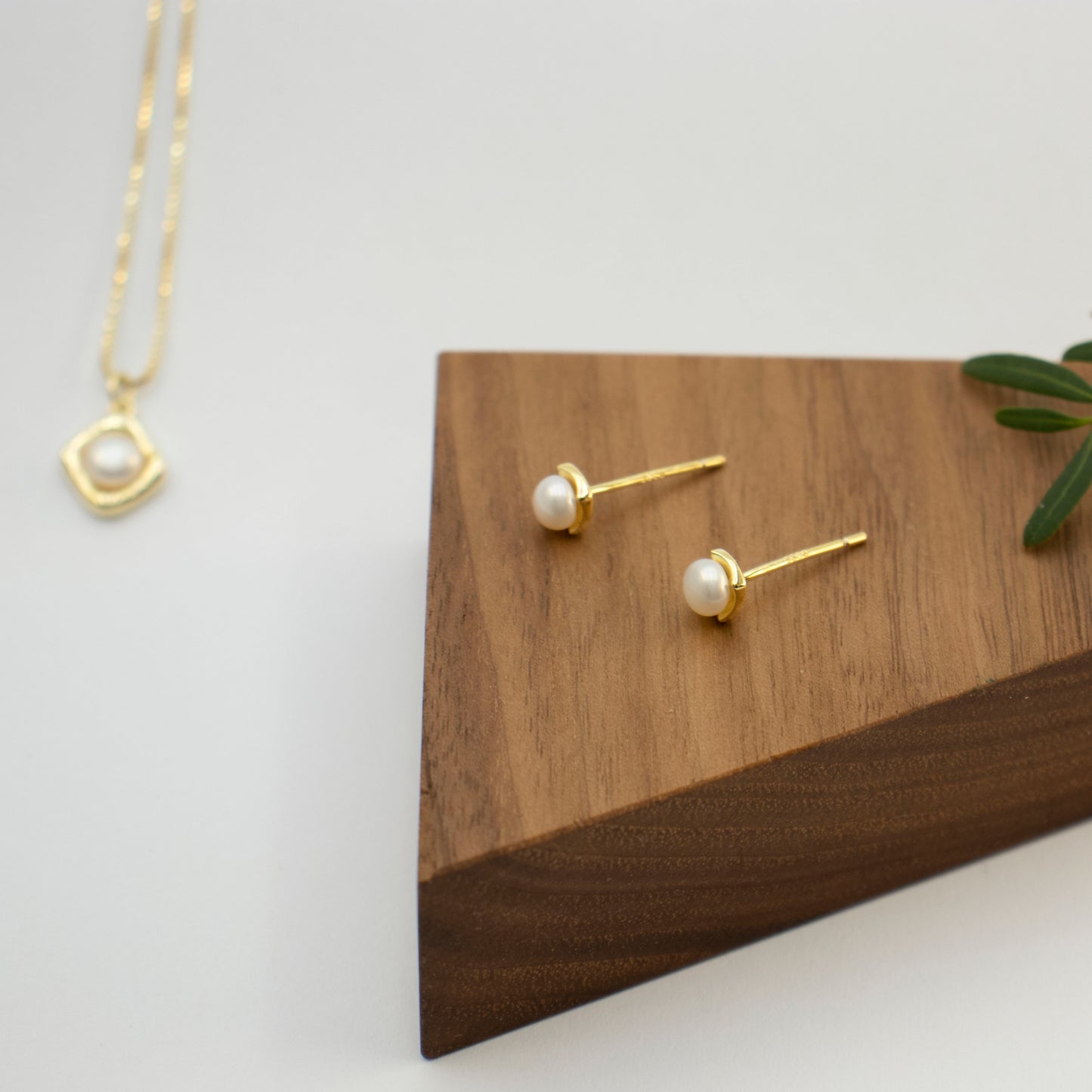 A rhombus stud earring embraces a button pearl.
