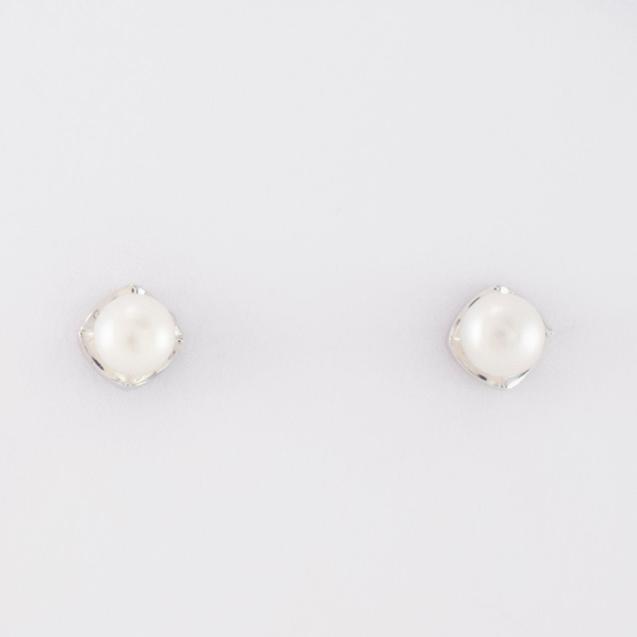 A rhombus stud earring embraces a button pearl.