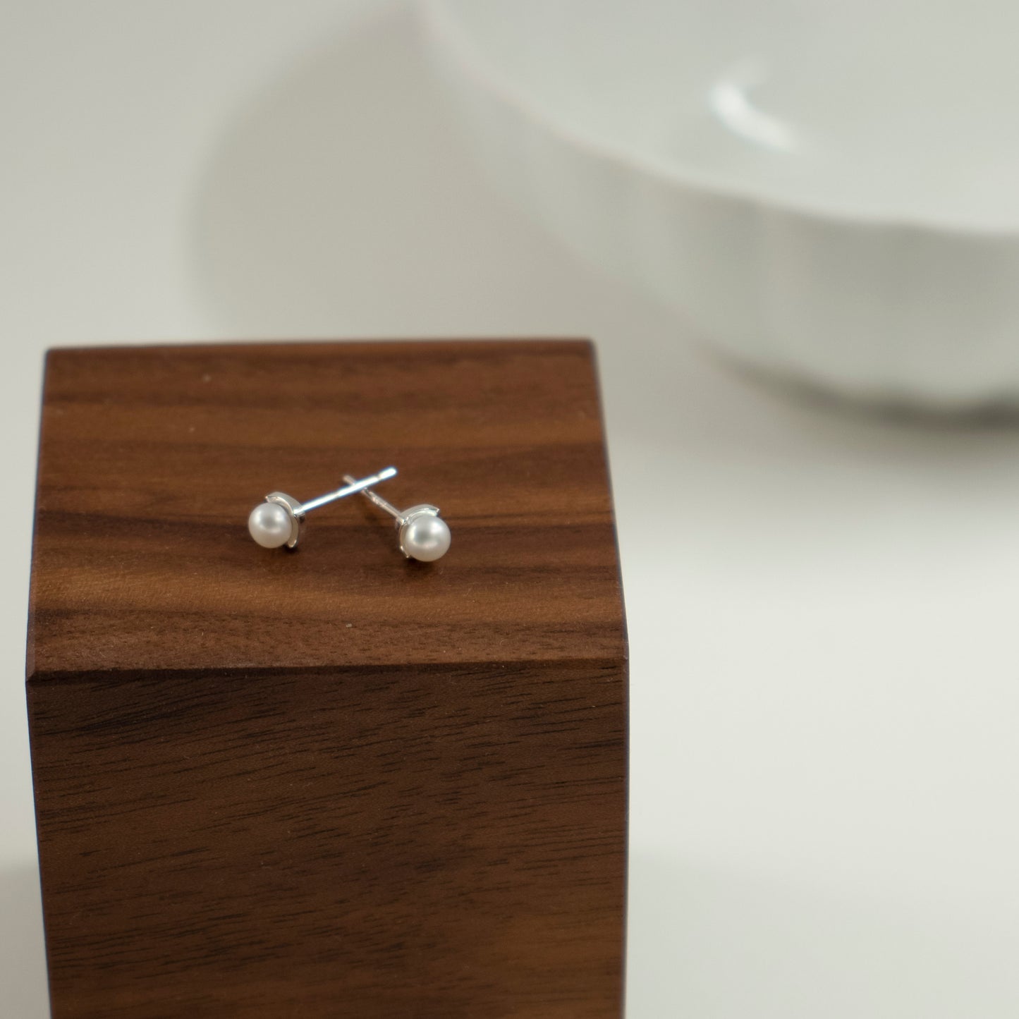 A rhombus stud earring embraces a button pearl.