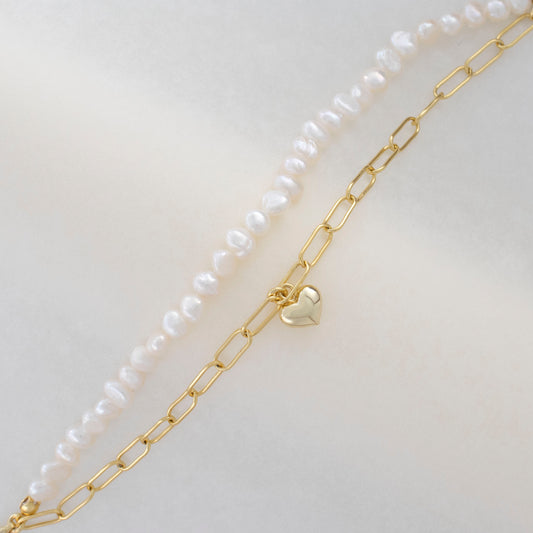 This stylish piece features a dual chain with baroque pearls and an alta chain with a heart pendant.